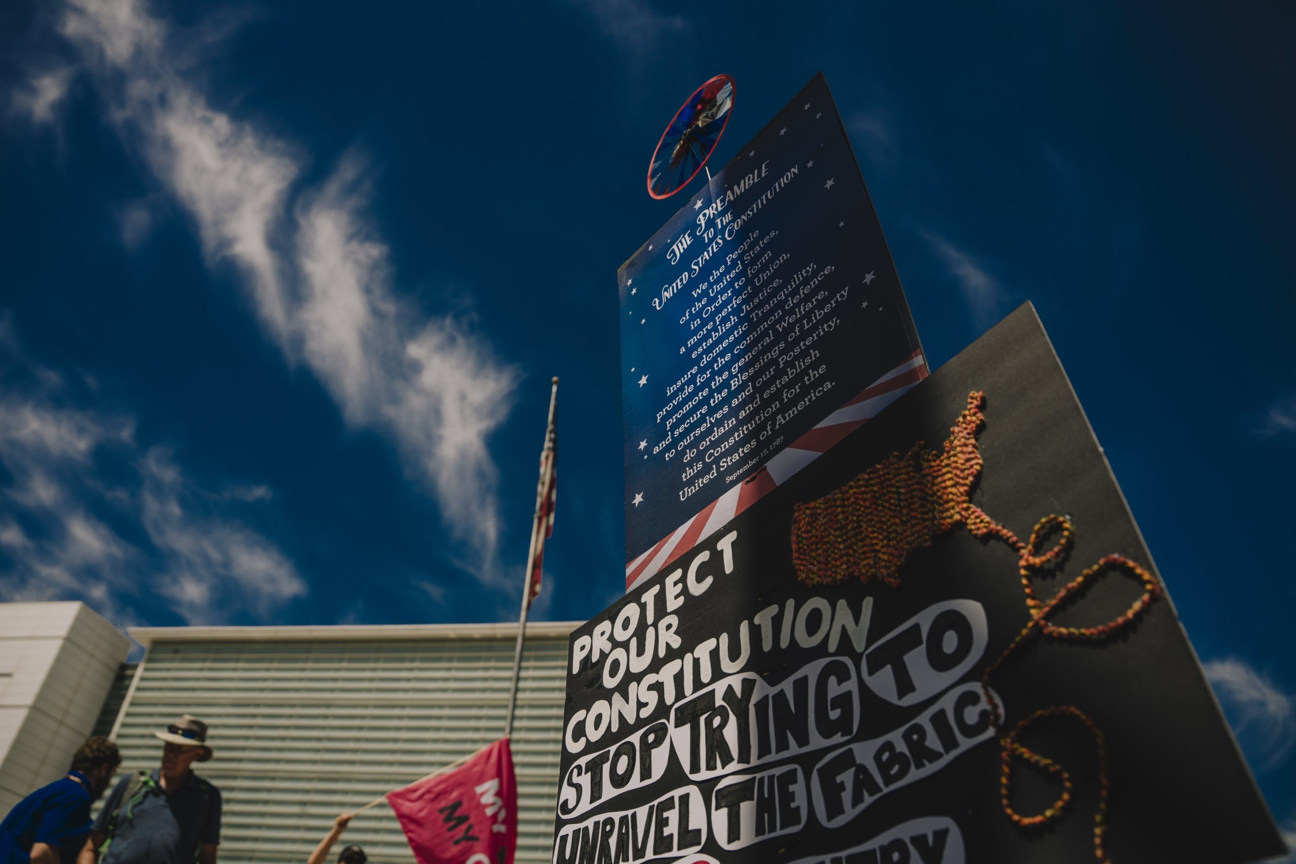 Protest signs against a partly cloudy deep blue sky.