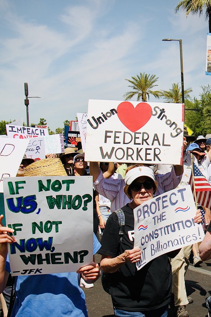 Protest march with about a dozen signs visible. Three are immediately readable: "Union" large read heart "Strong"; "FEDERAL WORKER" against white. "If not us, who?" "If not how, when", -JFK against white. "Protect the constitution" "NOT billionaires"
