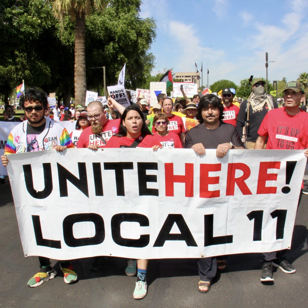 Protestors in front of a group marching with a sign that says "Unite here!" "Local 11"