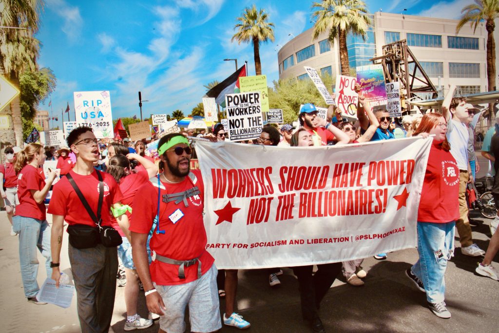 Protestors in front of a group wearing the same red shirt holding a sign that says "Workers should have power" "Not the billionaires" with information at the bottom: "Party for socialism and liberation | @pslphoenixaz"