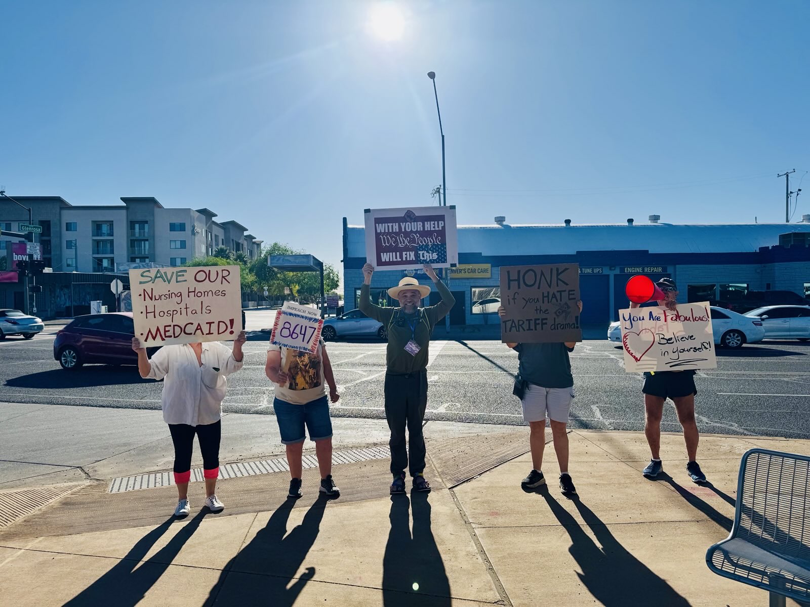 Five people standing in the day on a Phoenix street holding protest signs tailored to car drivers.